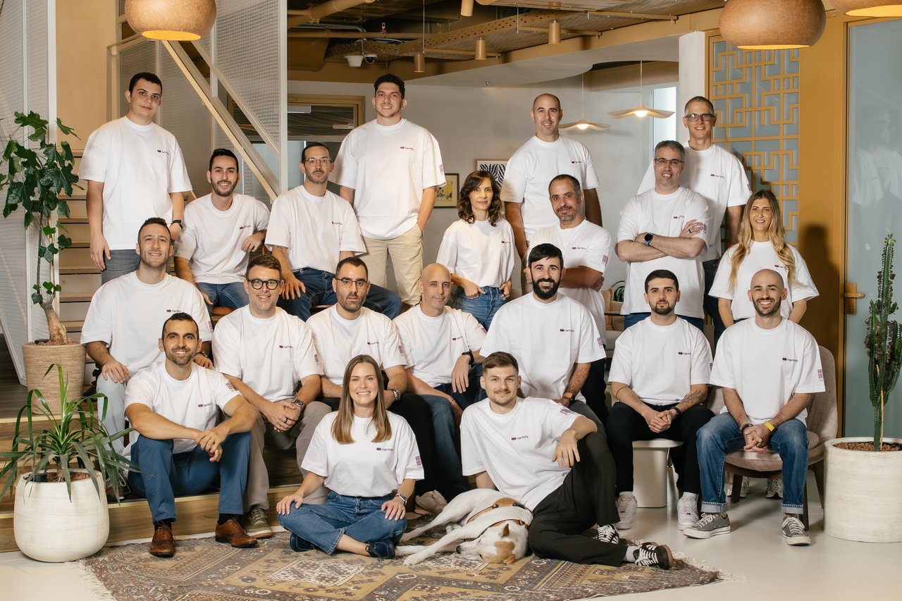 The Harmony.ai team, around thirty people in white Harmony.ai t-shirts, posing together in the office