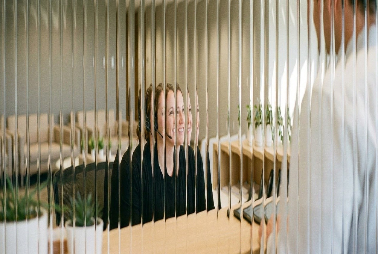 Smiling receptionist at a front desk behind fluted glass, standing in for the quick, friendly callback a new injury claimant gets from intake