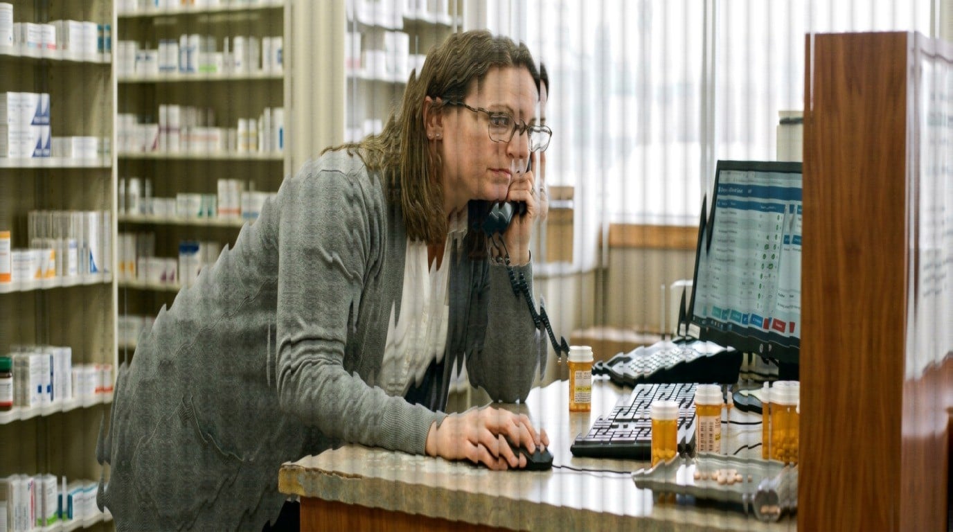 Pharmacist checking a prescription queue while taking a refill call